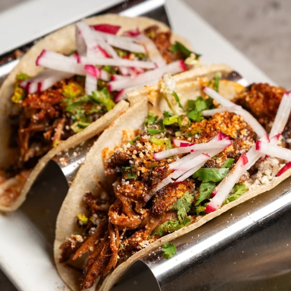 Two Laudy Bar Craft Kitchen tacos with shredded meat, radishes, cilantro, and cheese.