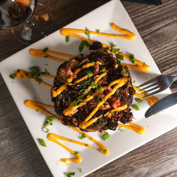 Crispy Brussels sprouts with bacon, orange sauce, and green onions on a white plate at Laudy Bar Craft Kitchen.