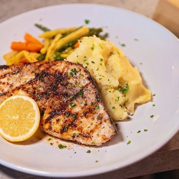 Grilled fish with a lemon slice, mashed potatoes, and mixed vegetables on a white plate.