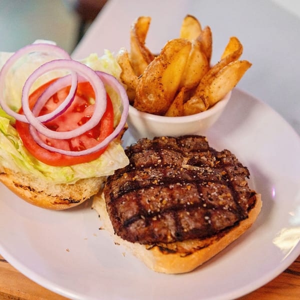 An open-faced burger with lettuce, tomato, and red onion, served with a side of potato wedges.