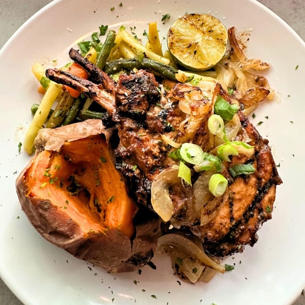 Grilled pork chop with baked sweet potato, green beans, and roasted onions on a white plate.