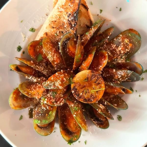 Mussels in a rich sauce with grilled lemon and toasted bread, garnished with cheese and herbs.