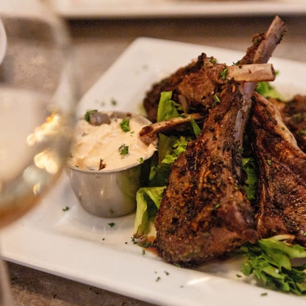 Grilled lamb chops with a side of mashed potatoes and green lettuce on a white plate.
