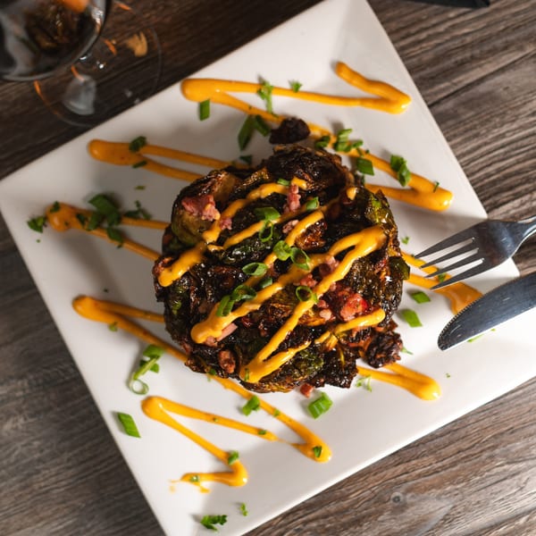 Crispy fried Brussels sprouts with orange sauce, bacon bits, and chives on a white plate.