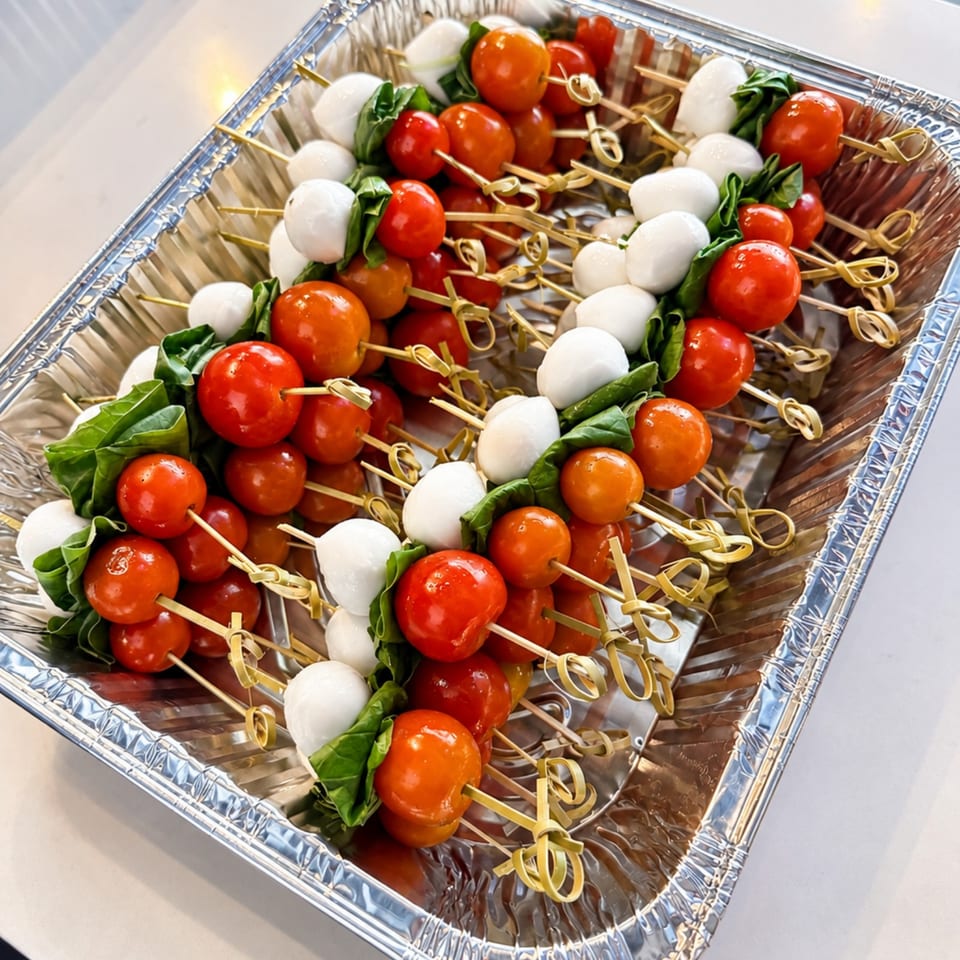 Tray of caprese skewers with cherry tomatoes, mozzarella balls, and fresh basil leaves.