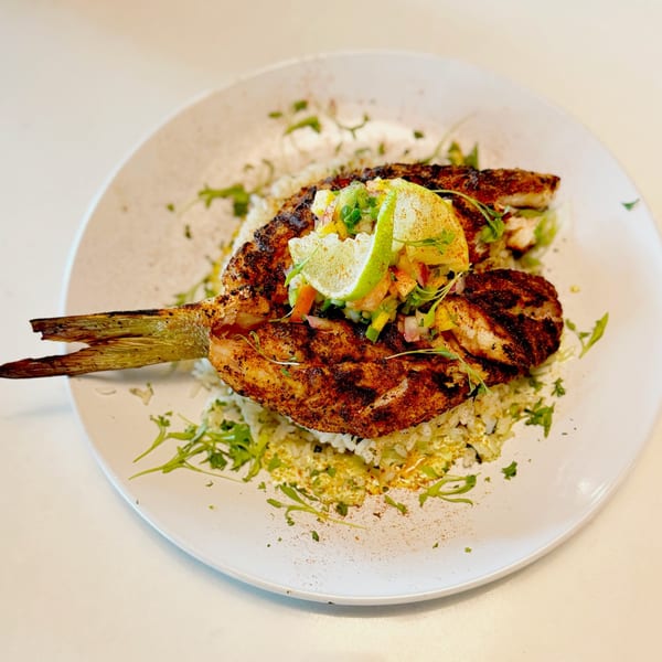 Grilled fish with a tail, topped with salsa and lime, served over rice on a white plate.