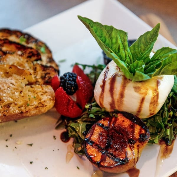 Grilled bread, burrata with basil, grilled peach, strawberries, and blackberries on a bed of greens.