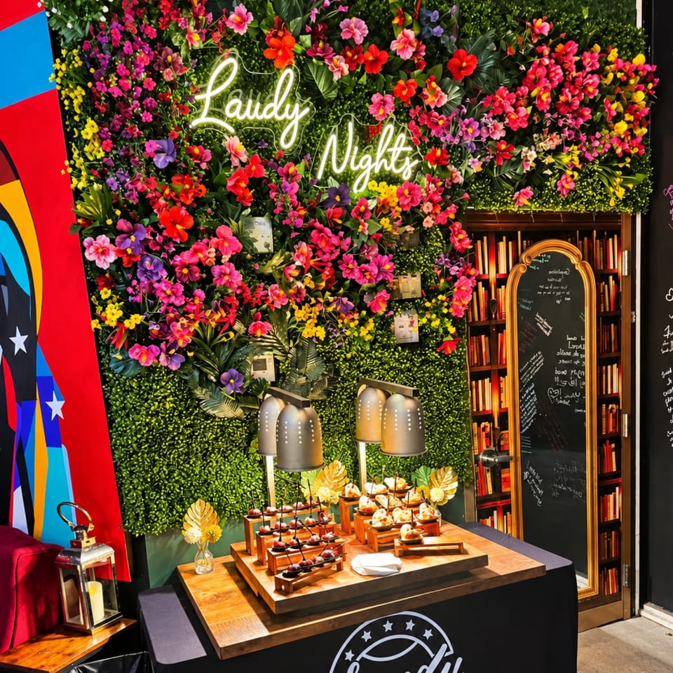 Colorful Lady Night event display with floral wall, neon sign, dessert table, lamps, bookshelf, and chalkboard menu.