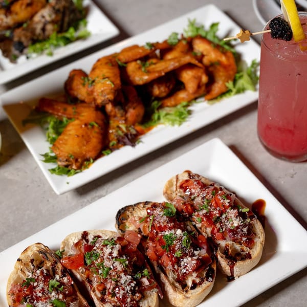 Plates of Laudy Bar Craft Kitchen's chicken wings and bruschetta, with a pink cocktail.